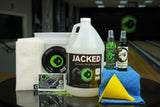 Image of Jacked Shredded Package: A 2.5 gallon bucket, a gallon of Jacked Continuous Motion Performance, CtD Absorption Pads, CtD Ball Cup, TruCut Scuff Mark Remover, 4 oz of That Wow Factor Hook Monster, 4 oz of Life After Death Ball Cleaner + Life Extender, a microfiber cloth and a funnel on a table in a bowling alley.