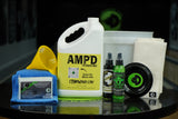 Image of AMP'D Angular Motion Performance Package on a table in a bowling alley. Contains one gallon of AMP'D, 4oz each of Life After Death Bowling Ball Cleaner Plus Life Extender and That Wow Factor HM, a CtD Ball Cup, one TruCut Scuff Mark Remover, one microfiber towel, two CtD Absorption Pads, a funnel, and a 2.5 gallon bucket.